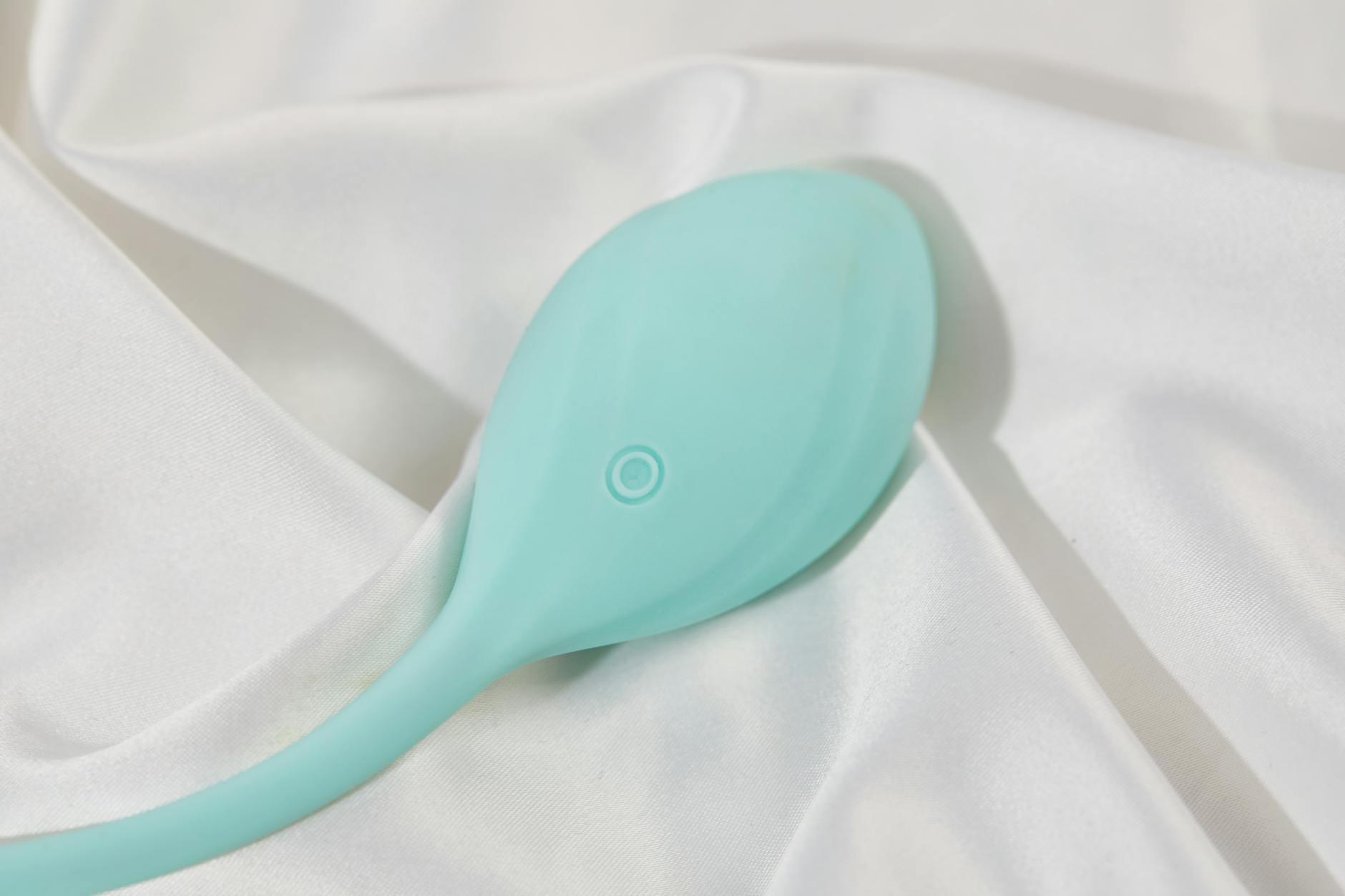 Un elegante vibratore teal su tessuto di seta bianca, perfetto per il benessere intimo consapevole
