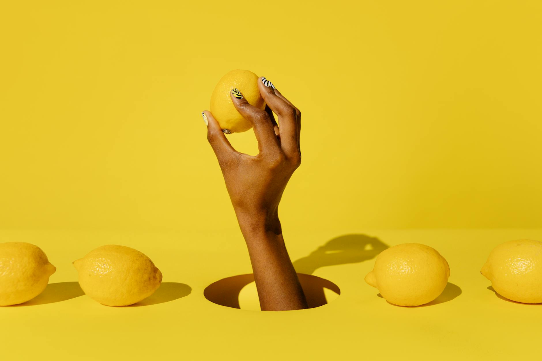 Mano che tiene un limone fresco su sfondo giallo vivido, evocando la freschezza e l'energia del Lem