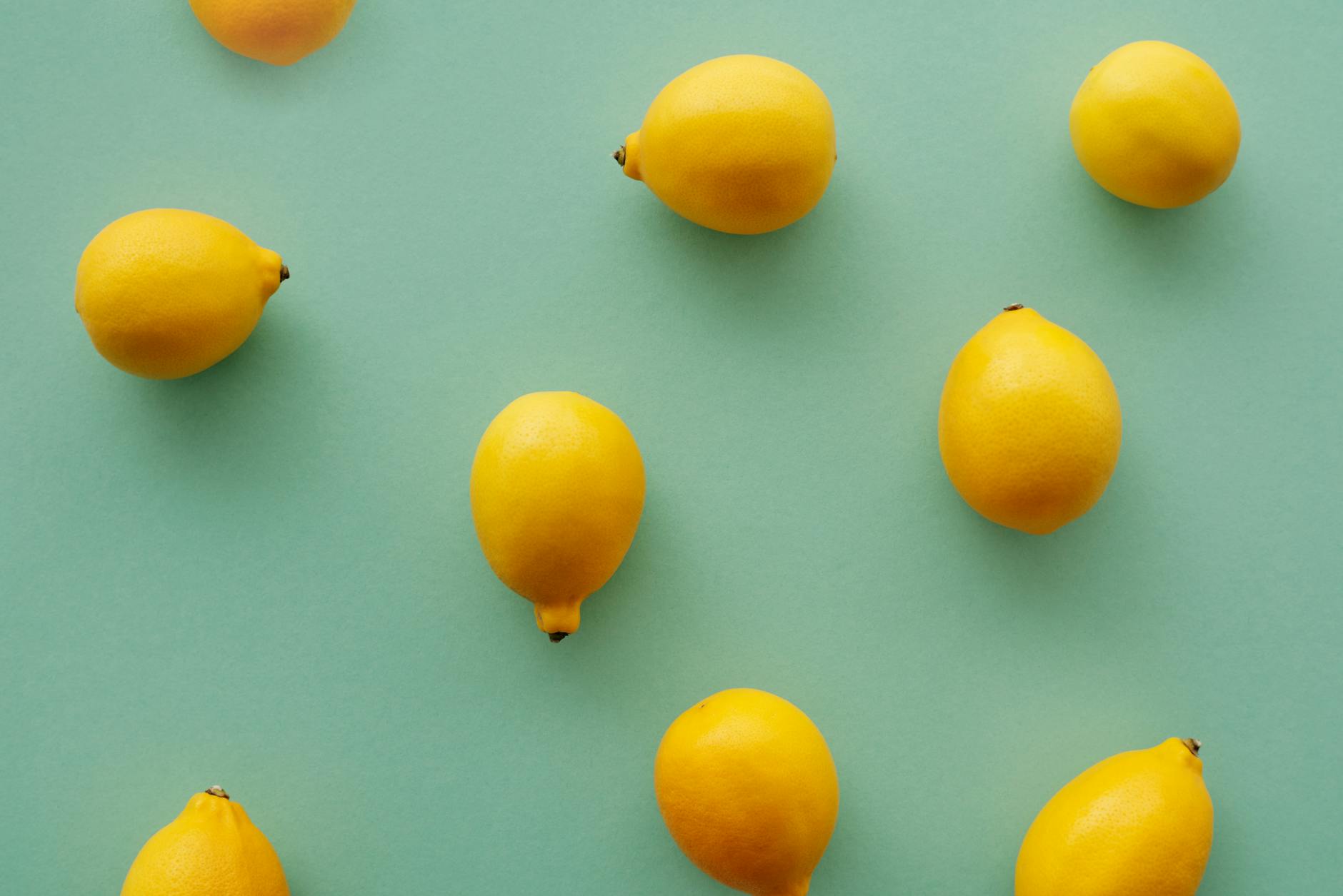Limoni freschi giallo brillante disposti su sfondo verde pastello, creando una composizione fresca e vibrante.