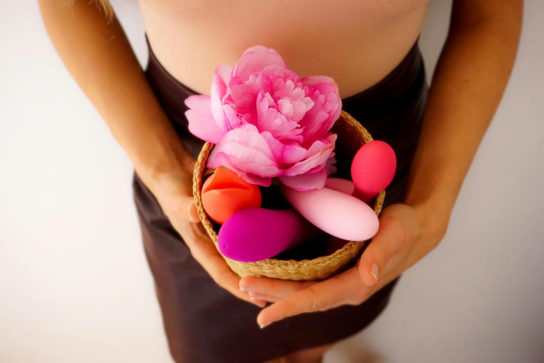 Persona che tiene un cesto con vibratori colorati e fiori rosa